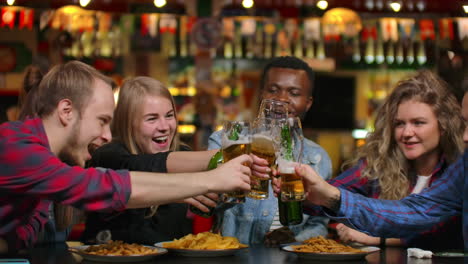 Close-up-plan-a-company-of-friends-makes-a-toast-and-everybody-knocks-check-their-glasses-with-beer-drink-and-laugh.-Students-meeting-in-a-bar-restaurant.
